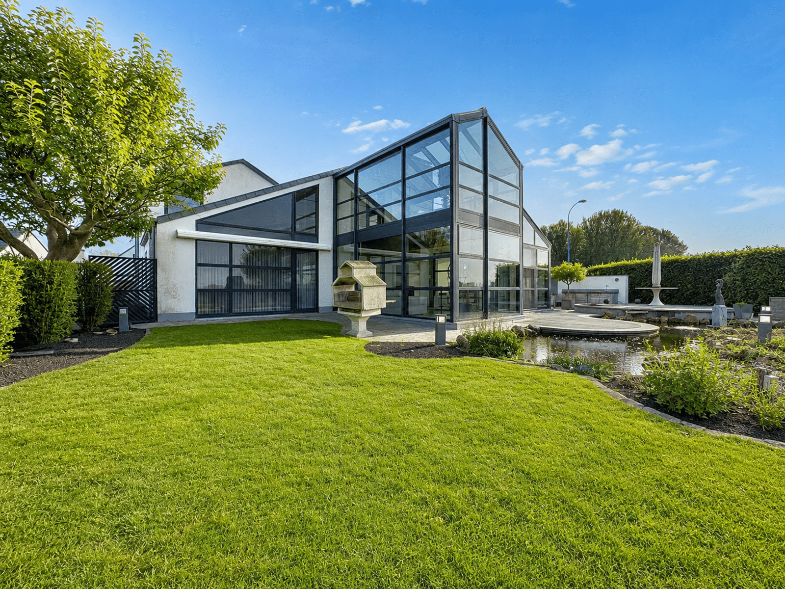Jardin Paysager avec Extension Vitrée – You Real Estate Agency Maison moderne avec extension vitrée, terrasse et jardin paysager.