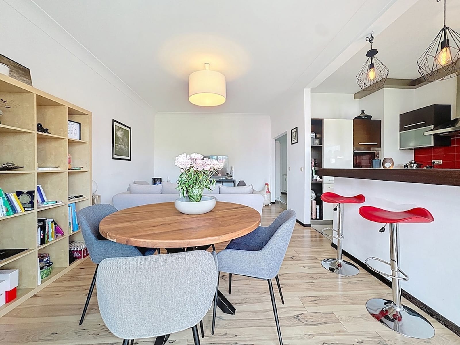 Bright Open Kitchen – You Real Estate Agency A modern apartment with an open kitchen, a bright dining room, and red stools.