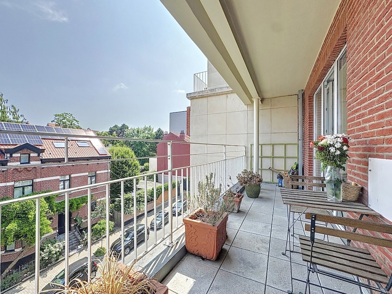 Balcony and Terrace with Residential View – You Real Estate Agency A bright apartment balcony/patio with a table, plants, and a view of the neighborhood.