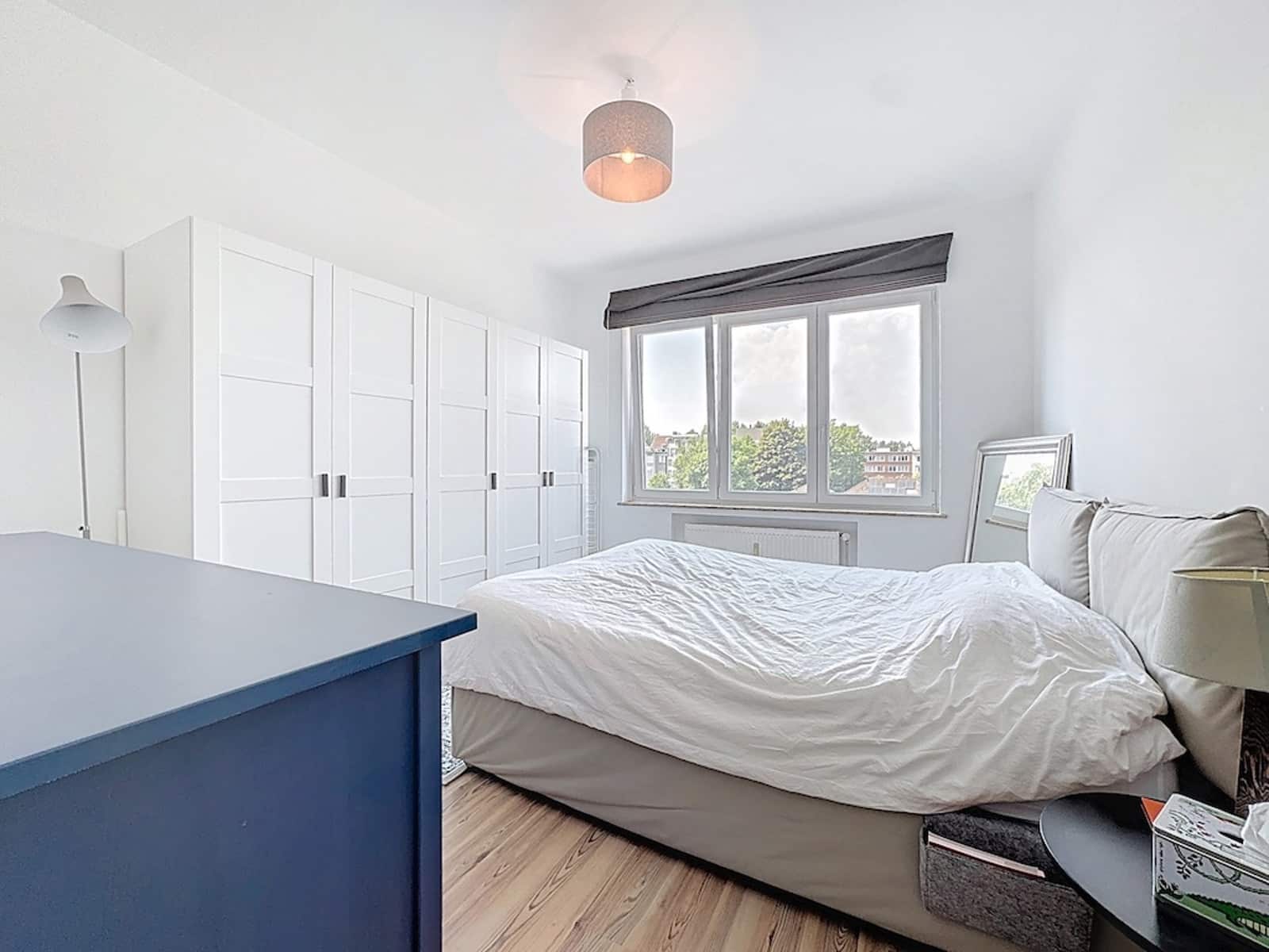 Bright bedroom with storage - You Real Estate Agency A bright apartment bedroom with built-in storage, a double bed, and a large window.