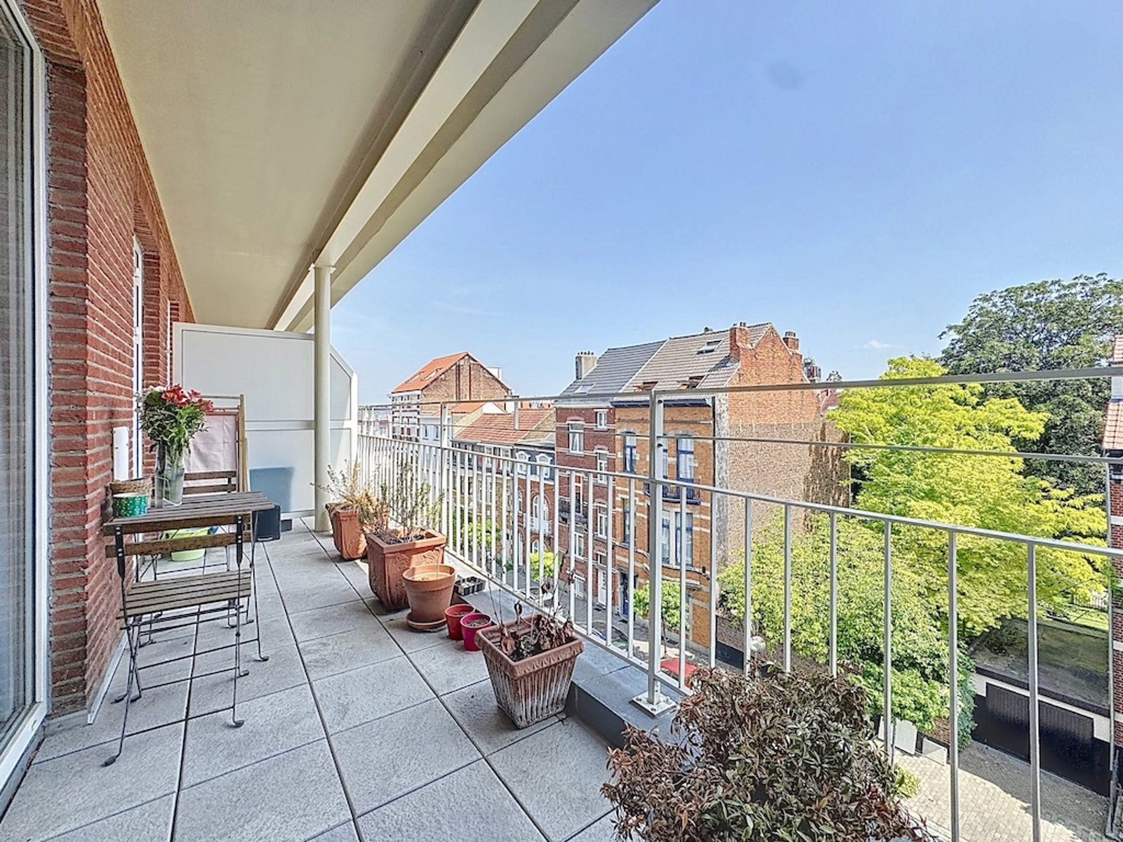 Covered Terrace with City Views – You Real Estate Agency Covered apartment terrace with a dining area, plants, and a city view.