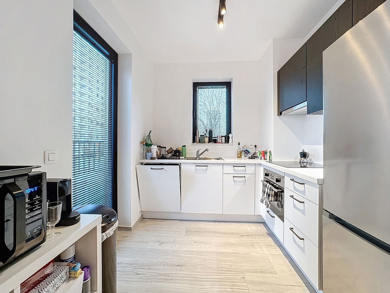 whise photo 5 Bright white modern kitchen with a window above the sink and light wood floors, stainless steel appliances visible on the right side.