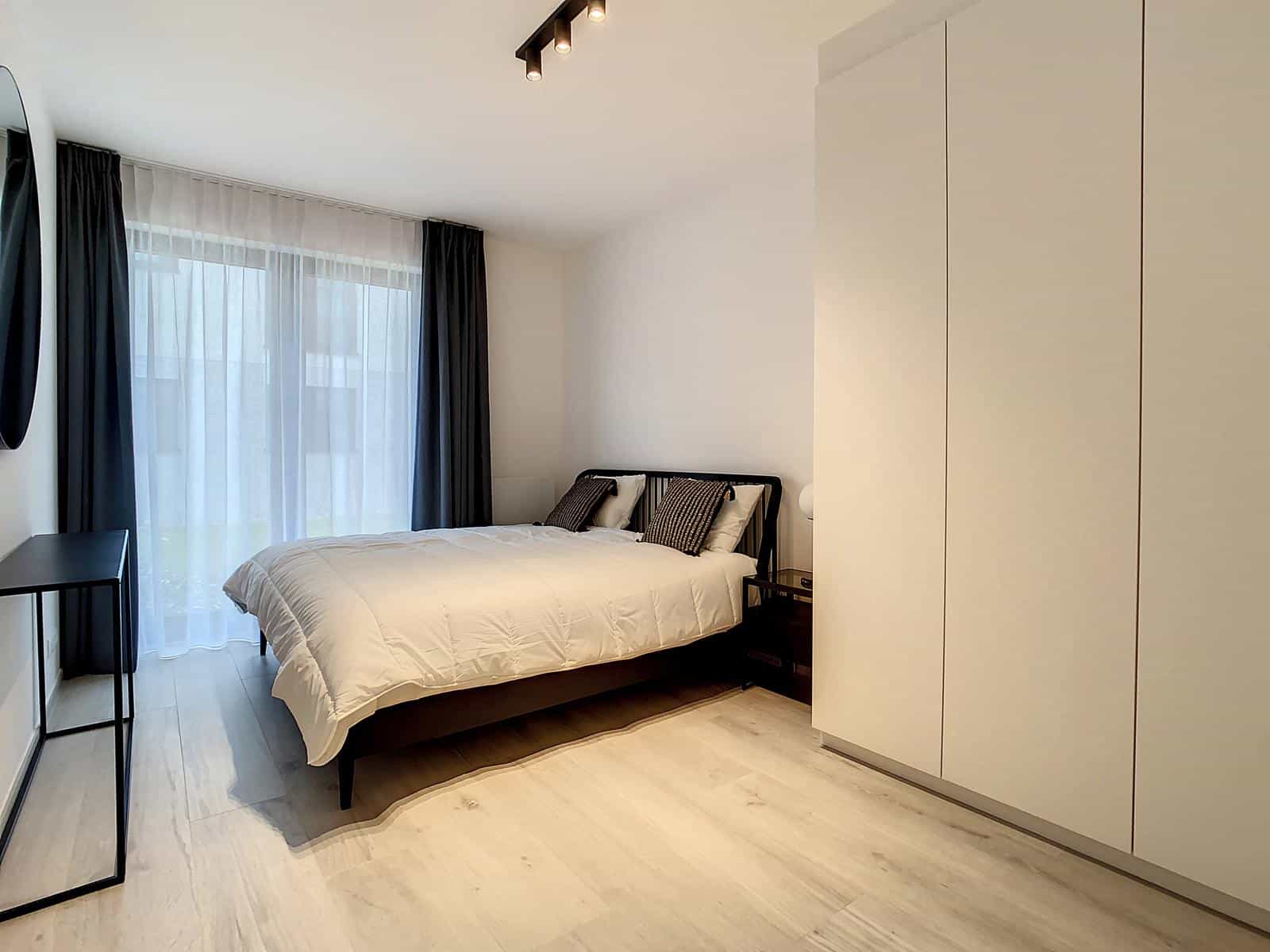 whise photo 5 Modern minimalist bedroom with white bedding on a black-framed bed, large white wardrobe, and sheer blackout curtains over a window.
