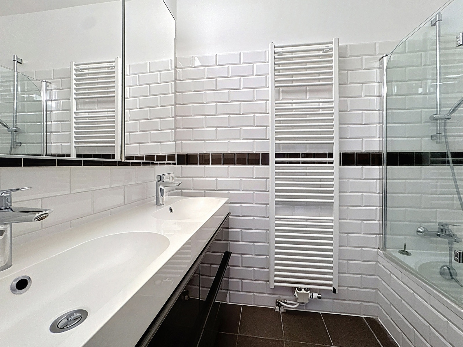 whise photo 9 Modern white-tiled bathroom with a double sink vanity and large mirror, featuring a wall-mounted heated towel rail and glass shower enclosure