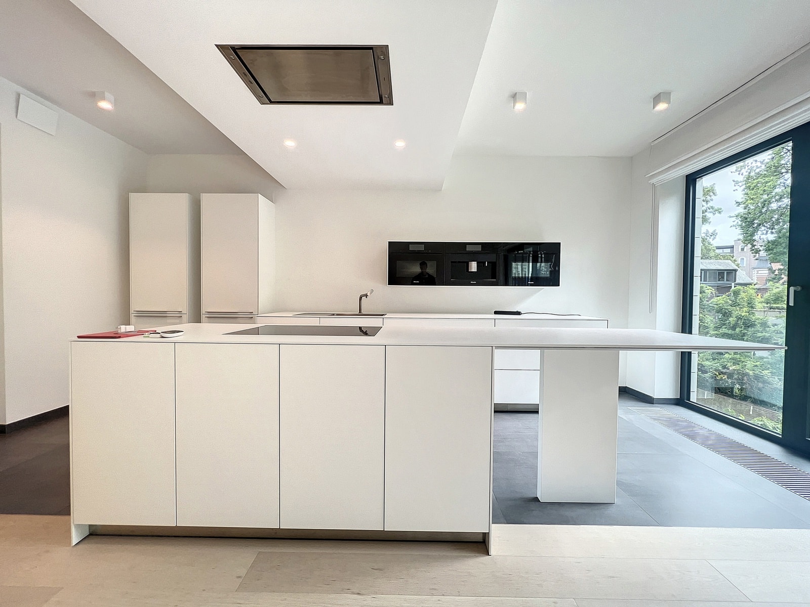 whise photo 6 Minimalist white kitchen with an island featuring an induction hob, sink, and handleless cabinets; large windows bring in natural light.