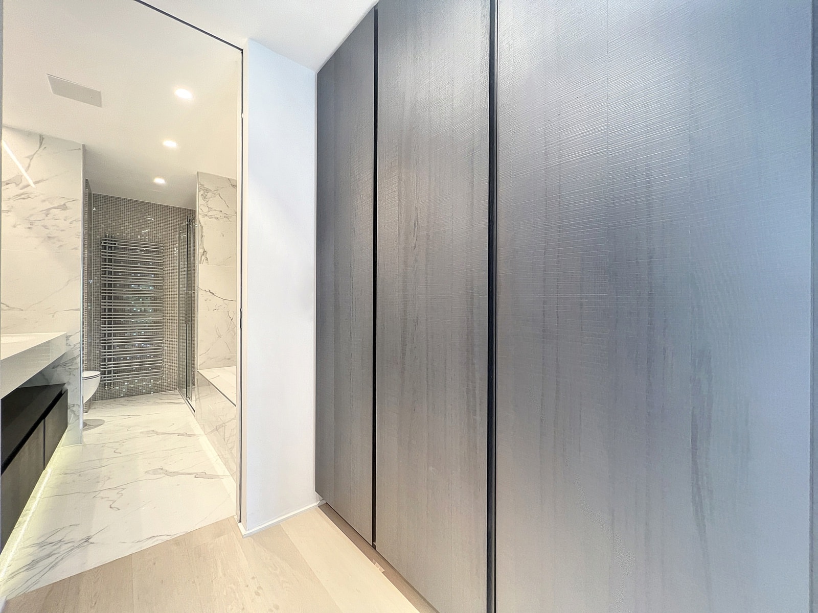 whise photo 13 Modern bathroom with marble walls, glass shower enclosure, and tall gray built-in cupboards along a hallway.