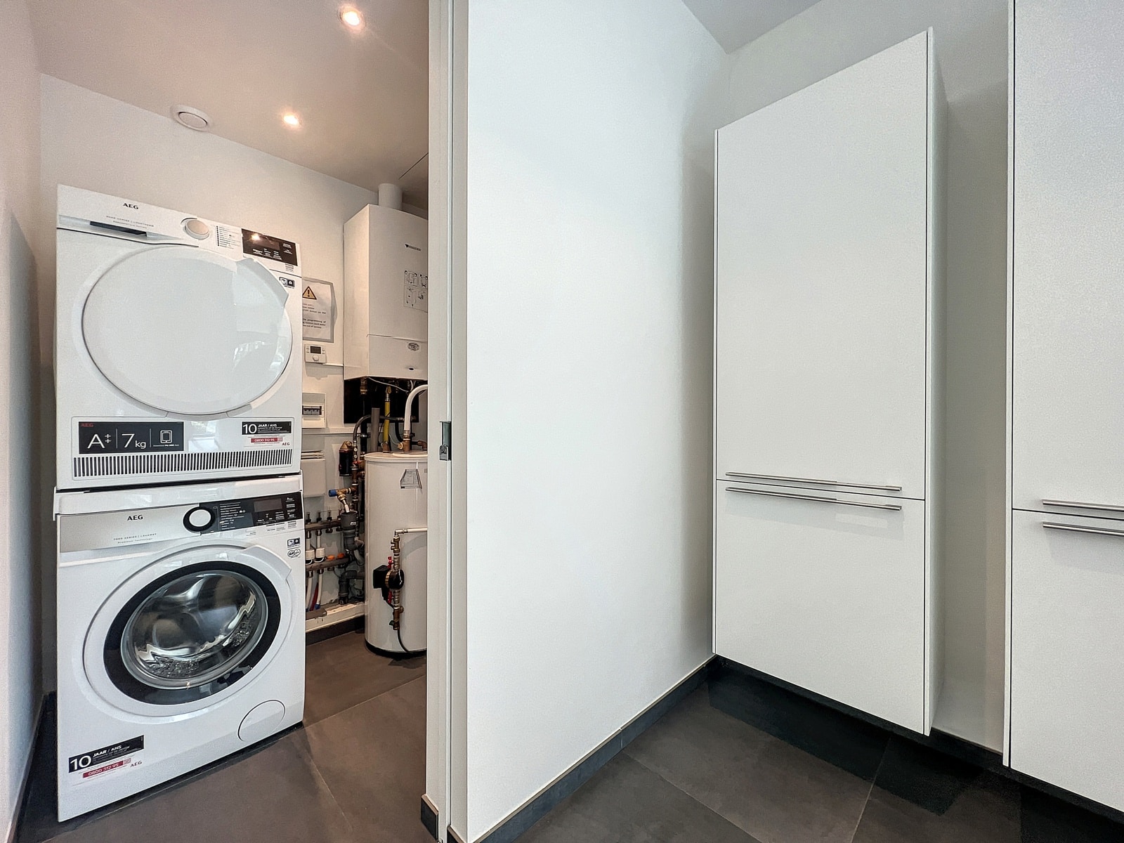 Buanderie Moderne Équipée – You Real Estate Agency Buanderie moderne d’appartement avec lave-linge, sèche-linge, chaudière et rangements intégrés.
