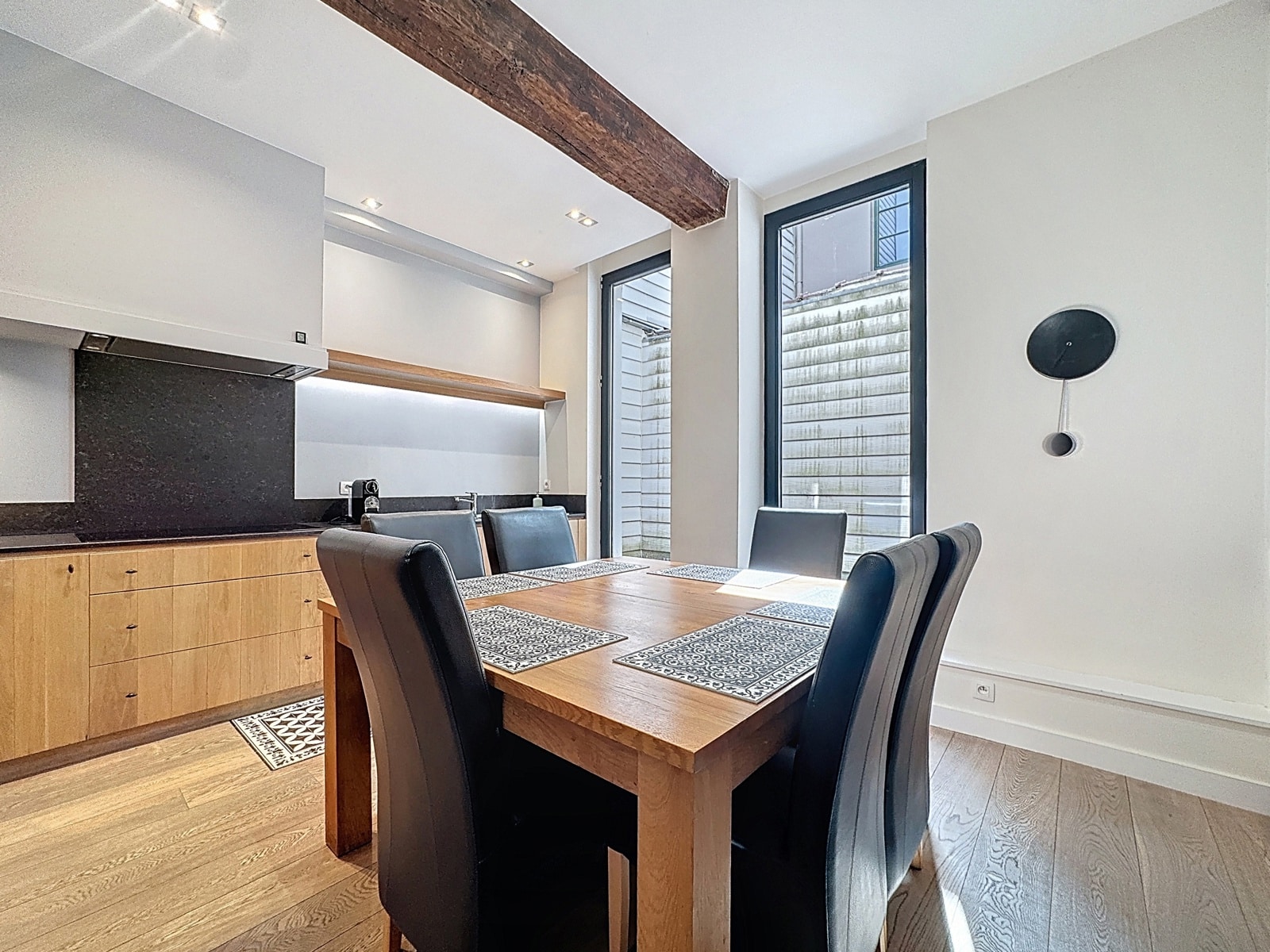 Salle à Manger avec Cuisine Ouverte – You Real Estate Agency Salle à manger moderne avec cuisine ouverte, table en bois et grandes fenêtres.