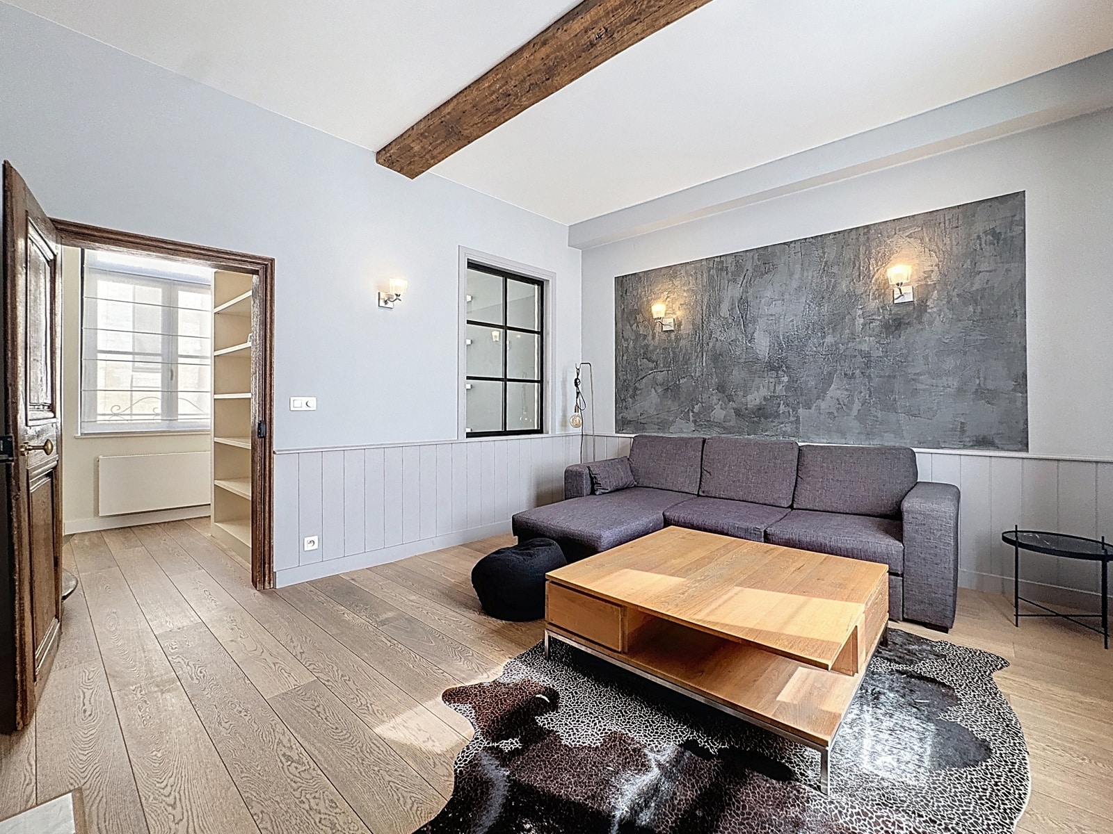 Salon Moderne avec Poutre Apparente – You Real Estate Agency Salon moderne lumineux avec canapé gris, poutre apparente et parquet en bois.