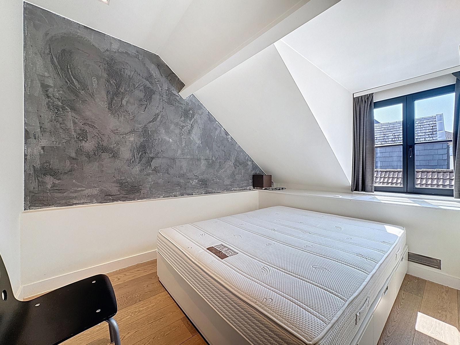 Chambre Mansardée avec Mur Texturé – You Real Estate Agency Chambre mansardée moderne dans appartement, mur texturé gris et lit intégré.