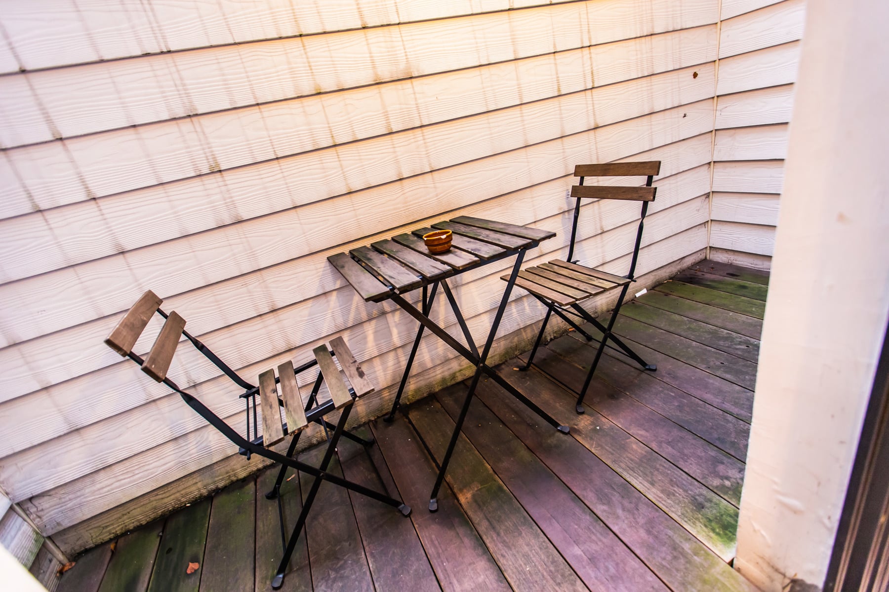 Petite Terrasse en Bois – You Real Estate Agency Petite terrasse en bois avec table bistrot et chaises pliantes.