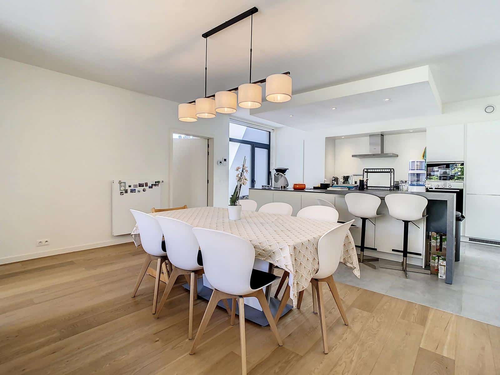 foto 7 Een open eet- en keukengedeelte met een lange tafel, zes witte stoelen en een rij hanglampen erboven.