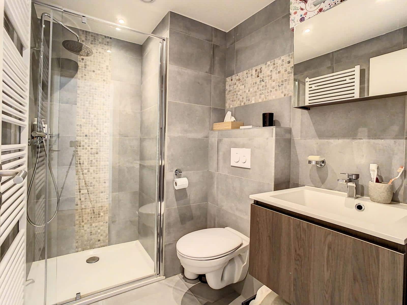 Wijze foto 11 Moderne badkamer met glazen douchecabine, grijze tegelwanden, een hangend toilet en een houten wastafelmeubel.