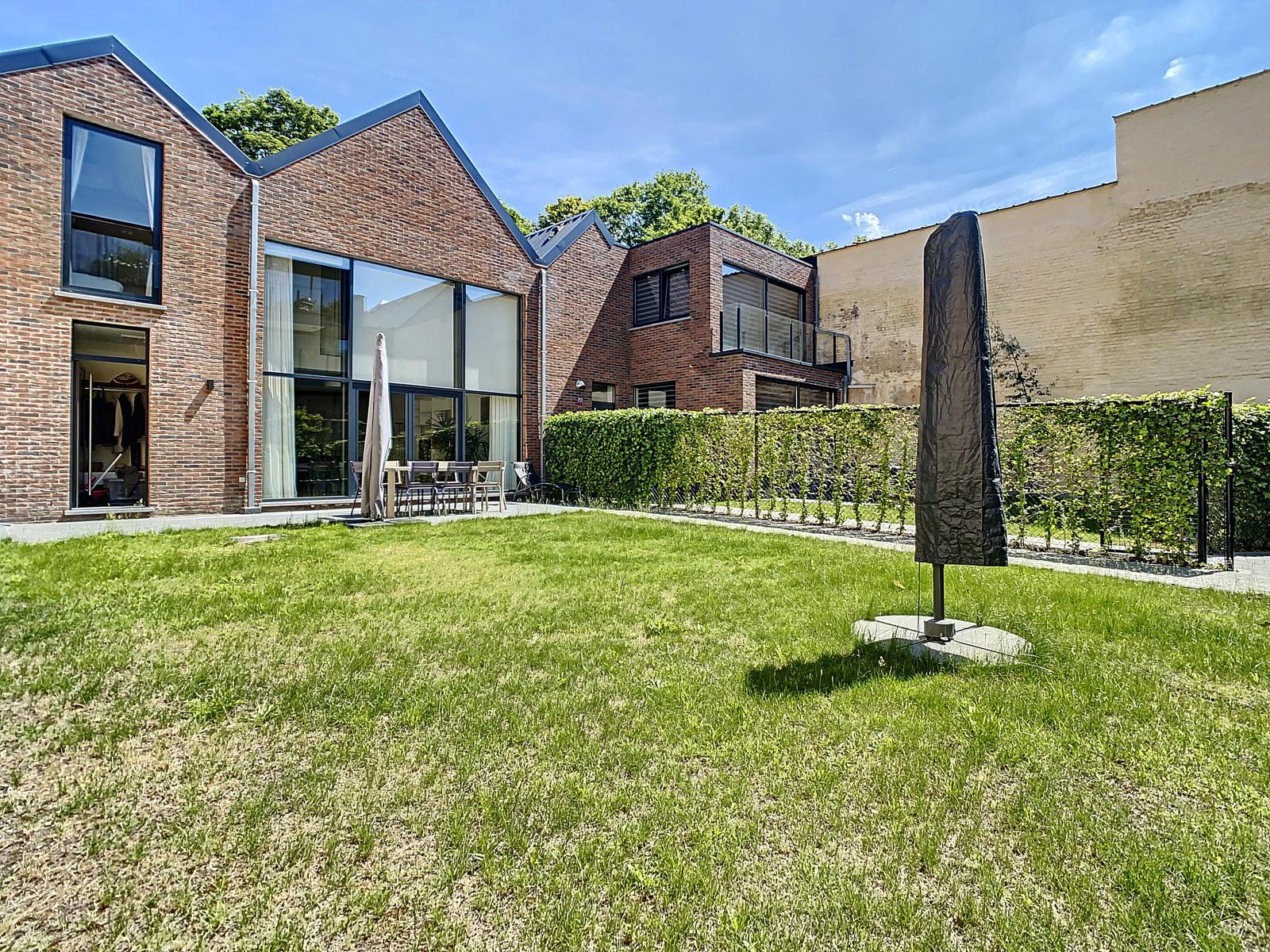 Achtergevel met tuin - U Vastgoedkantoor Moderne bakstenen woning met grote tuin, terras en grote ramen.