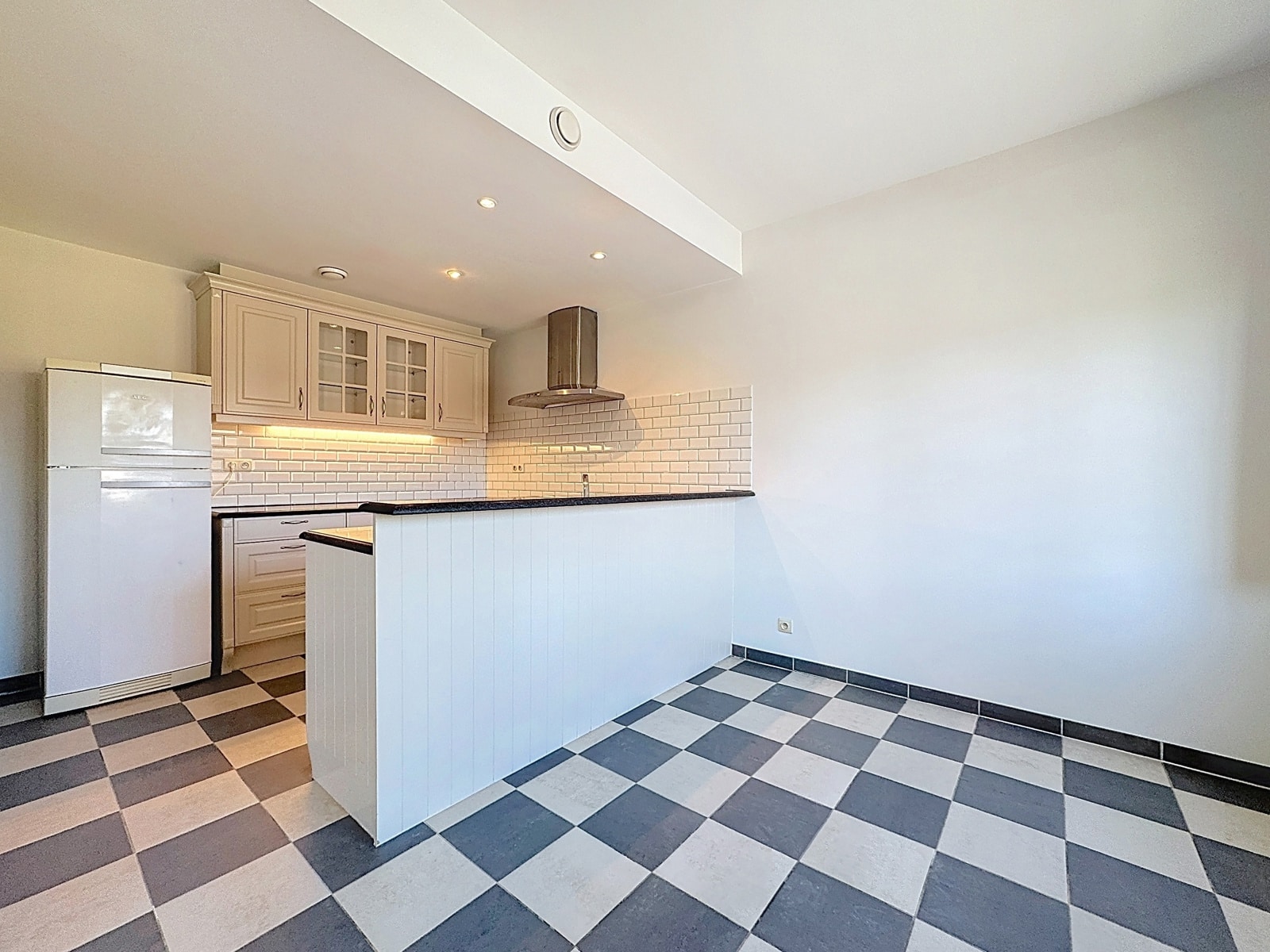 foto 4 Bright white kitchen with checkered gray and white floor, white island, and wall cabinets with glass-front doors.