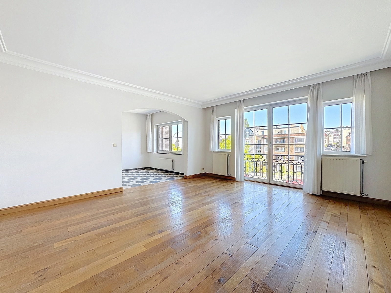 Lichte woonkamer met parketvloer - You Real Estate Agency Lichte woonkamer met parketvloer, grote ramen en een balkon in een gerenoveerd appartement.
