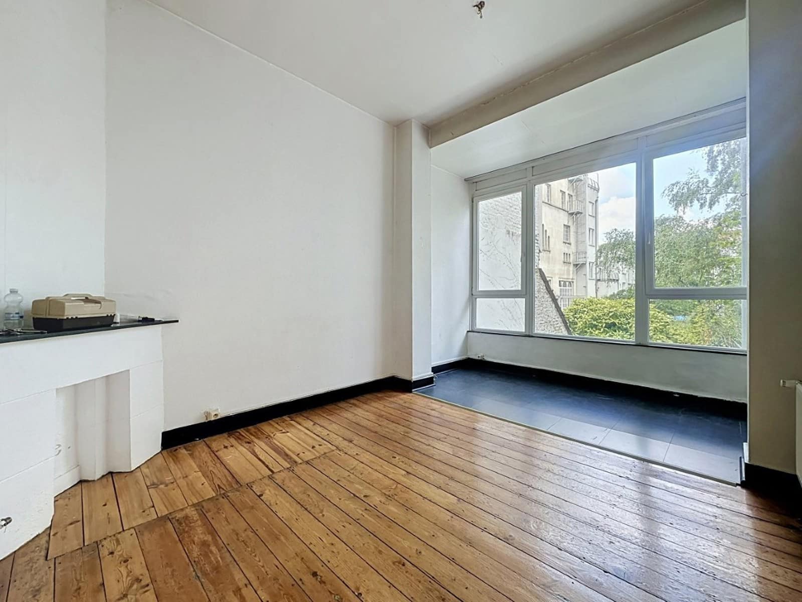 Salon Lumineux avec Cheminée – You Real Estate Agency Salon lumineux d’appartement avec parquet ancien, cheminée et grande baie vitrée.