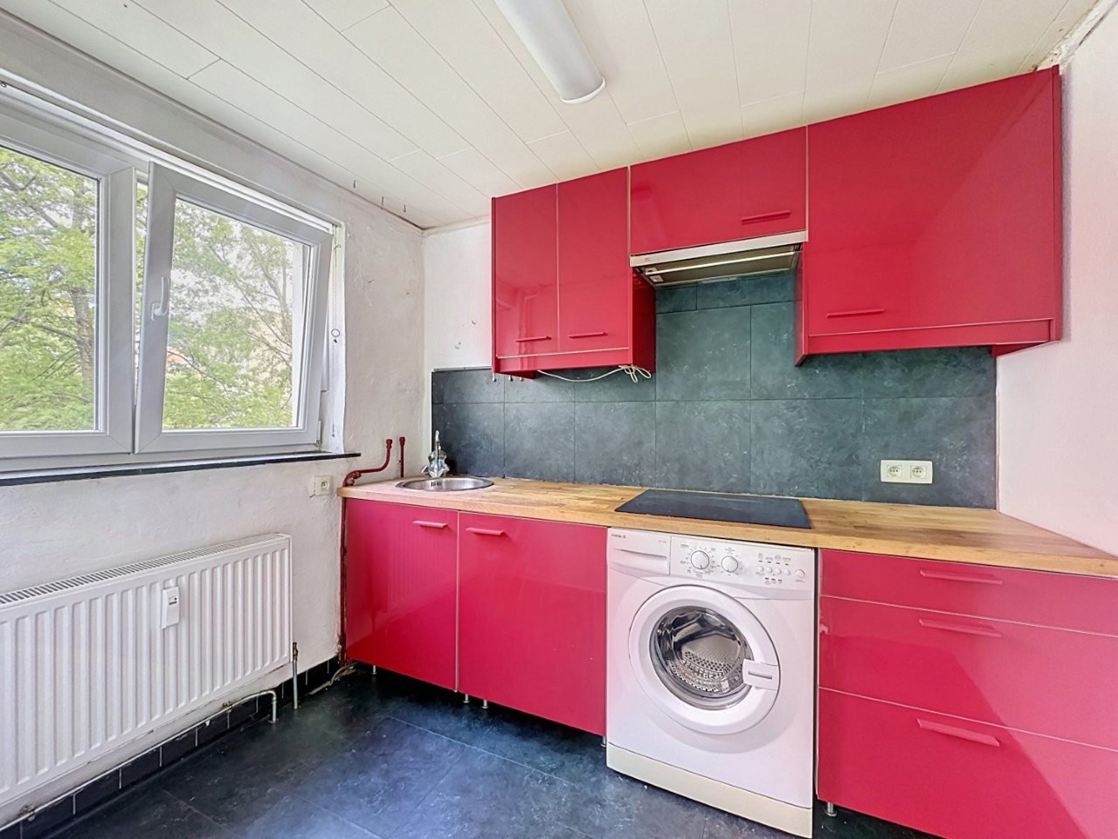 whise photo 3 Bright pink kitchen with glossy upper and lower cabinets, wooden countertop, grey tile backsplash, and a front-loading washing machine under the counter.