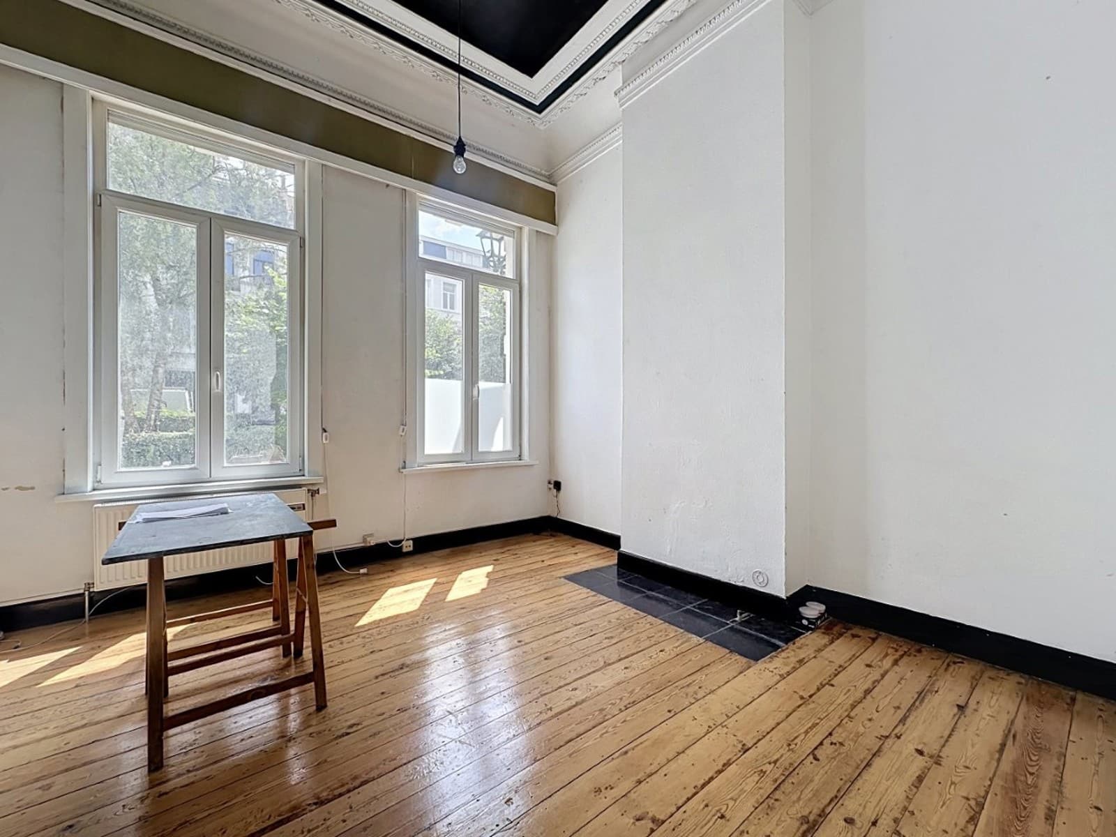 whise photo 5 Bright, empty room with tall windows, white walls, and a wooden floor; a small wooden table sits by the window.