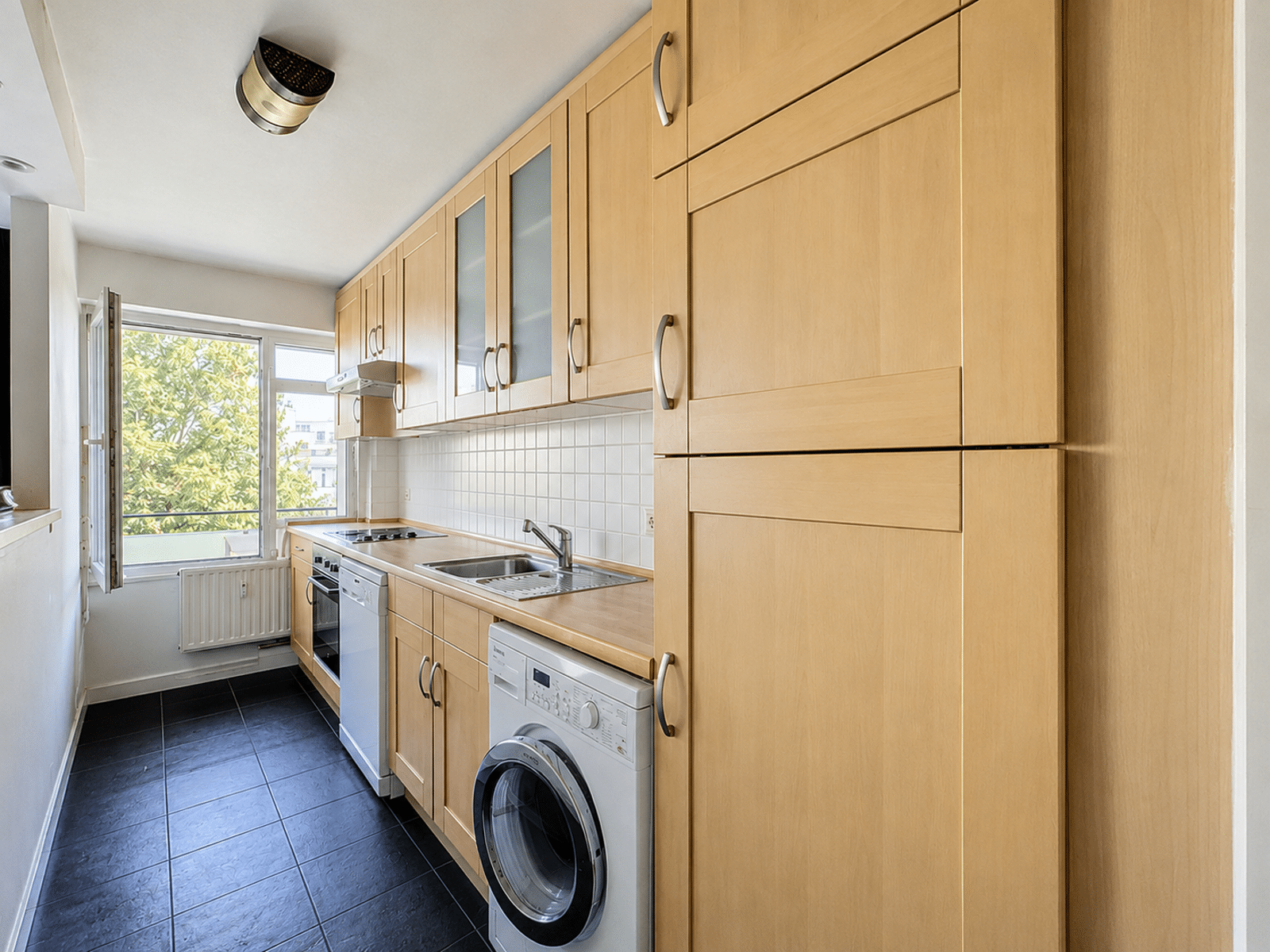 Lichte ingerichte keuken - U Vastgoedkantoor Lichte, volledig ingerichte keuken in een appartement met houten opbergkasten en een open raam.