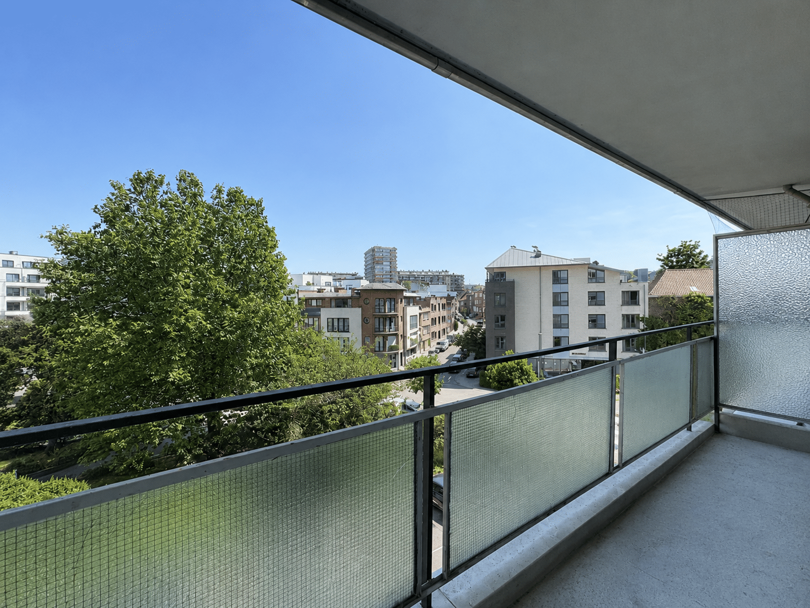 Terras met uitzicht op de bomen – You Real Estate Agency Terras bij een appartement met vrij uitzicht op een groene woonwijk.