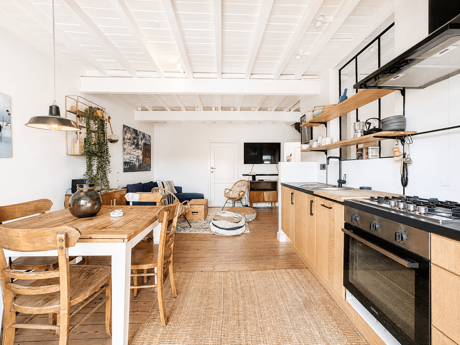 whise photo 7 Bright open-concept kitchen and living area with a wooden dining table, chairs, shelves, and a blue sofa under white ceiling beams.