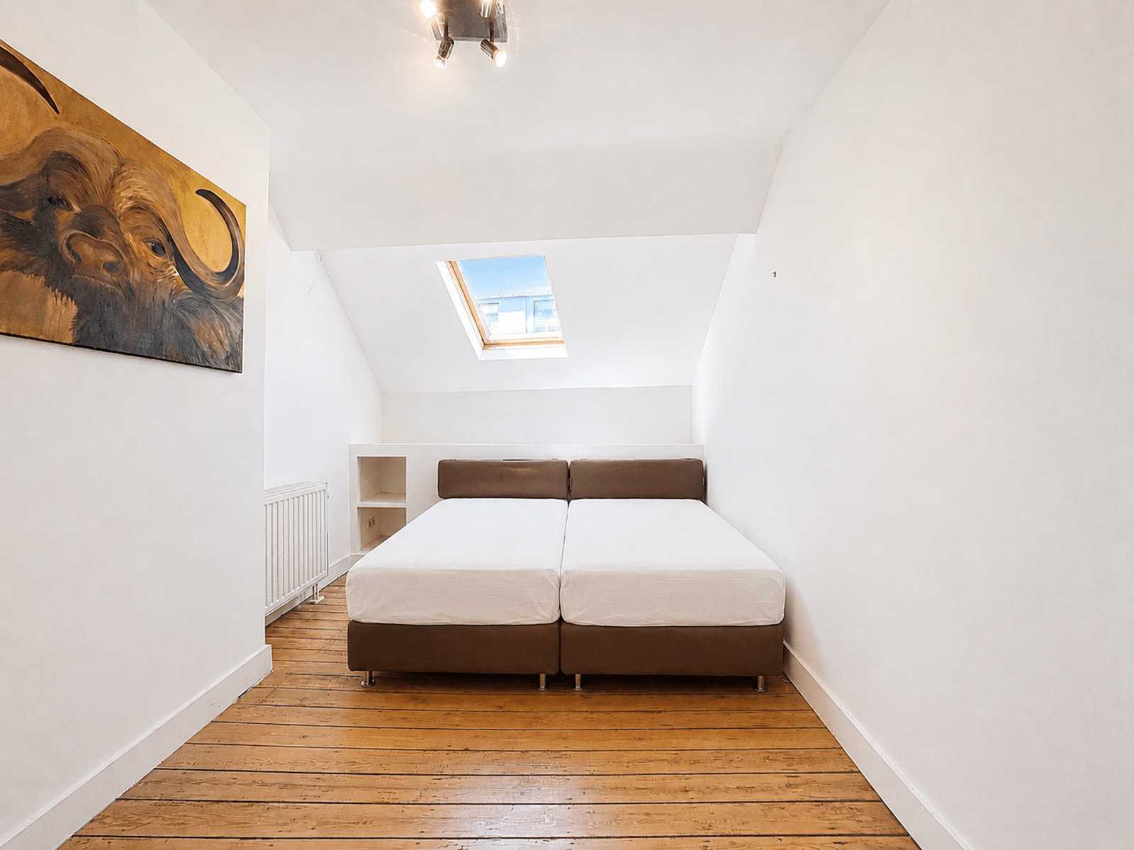 Chambre Mansardée Lumineuse – You Real Estate Agency Chambre mansardée lumineuse avec deux lits, parquet et fenêtre de toit dans appartement.