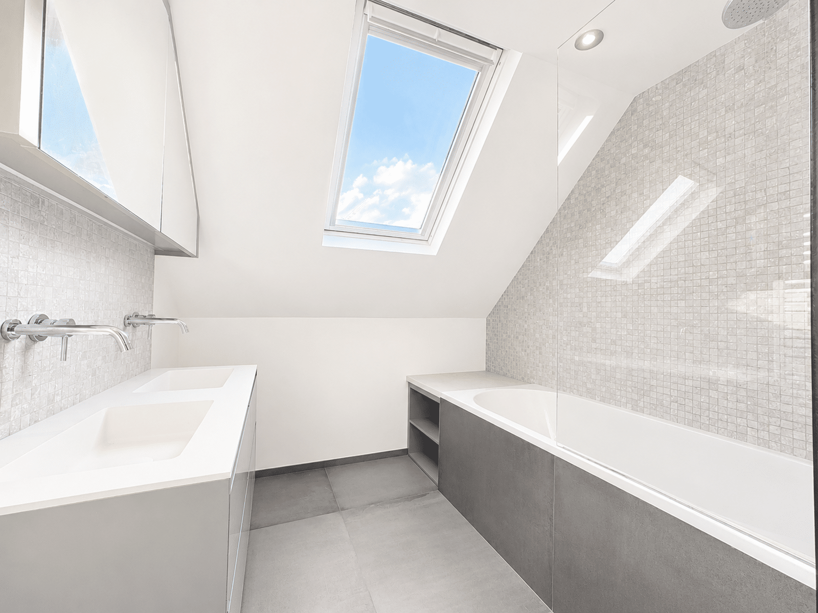 Salle de Bain Lumineuse Sous Combles – You Real Estate Agency Salle de bain moderne sous combles avec baignoire, double vasque et puits de lumière.