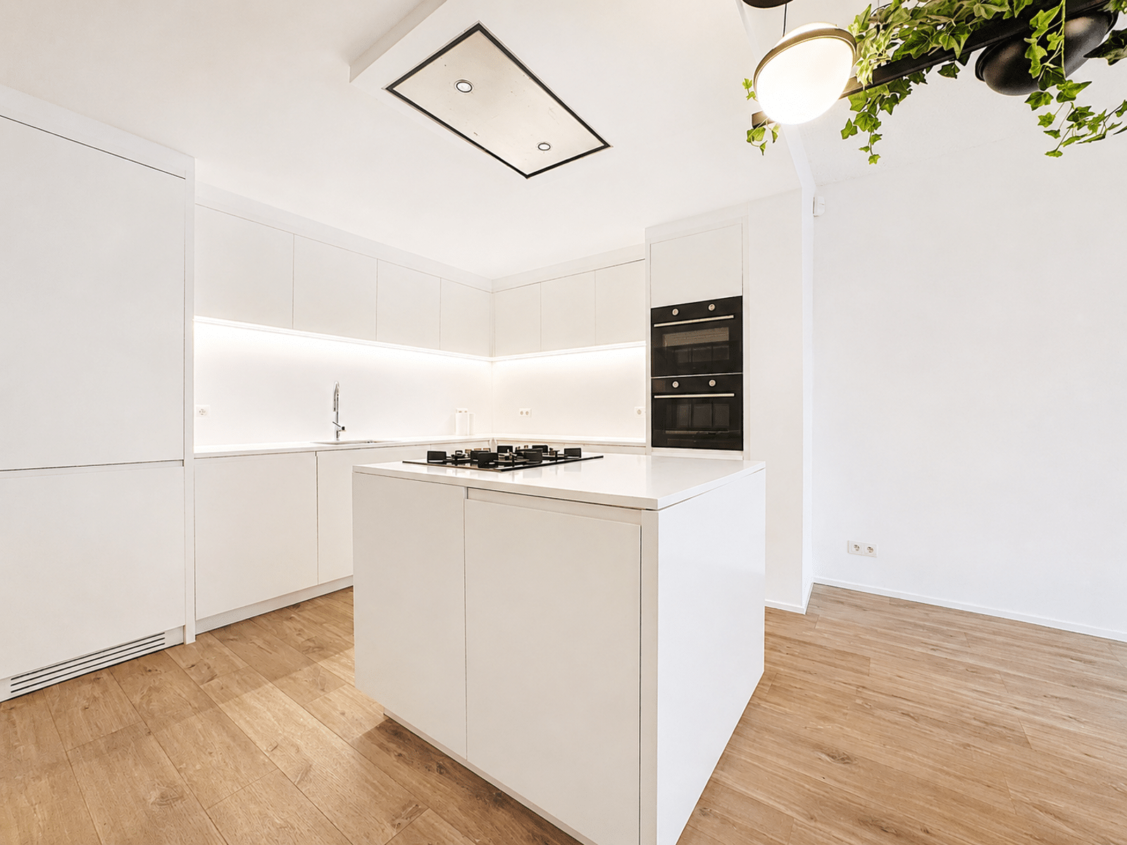 Cuisine Moderne avec Îlot – You Real Estate Agency Cuisine moderne blanche avec îlot central, électroménager encastré et parquet clair.