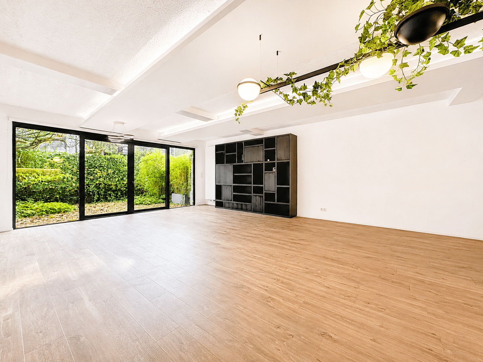 Salon Lumineux avec Jardin – You Real Estate Agency Salon d’appartement lumineux avec parquet, baies vitrées sur jardin et étagères intégrées.