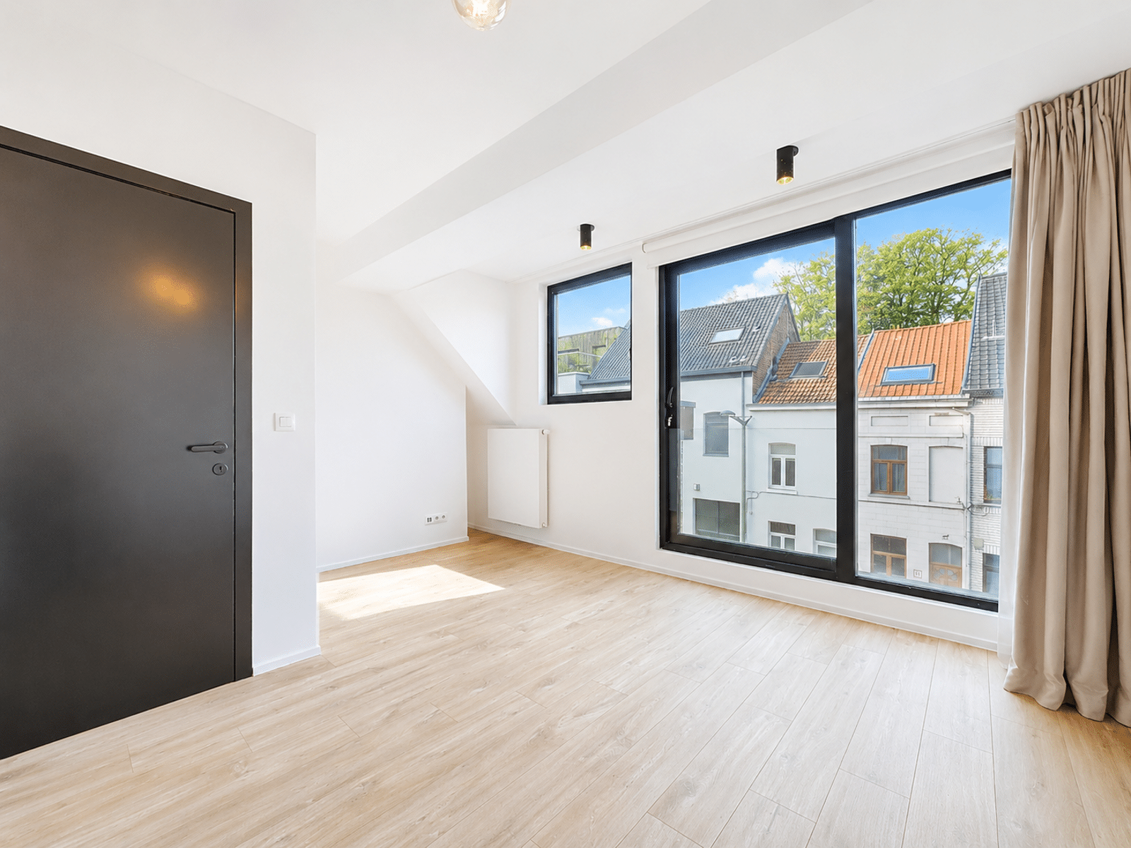 Pièce Lumineuse avec Grandes Fenêtres – You Real Estate Agency Appartement lumineux avec parquet, grandes fenêtres et porte noire moderne.