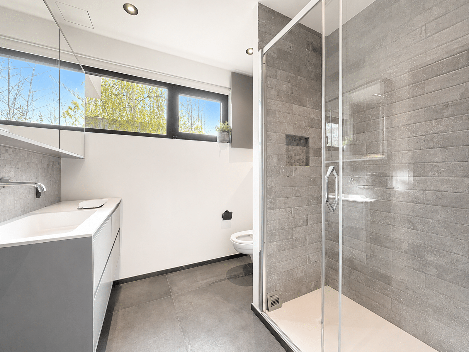 Salle de Bains Moderne et Lumineuse – You Real Estate Agency Salle de bains moderne avec douche vitrée et meuble vasque dans appartement lumineux.