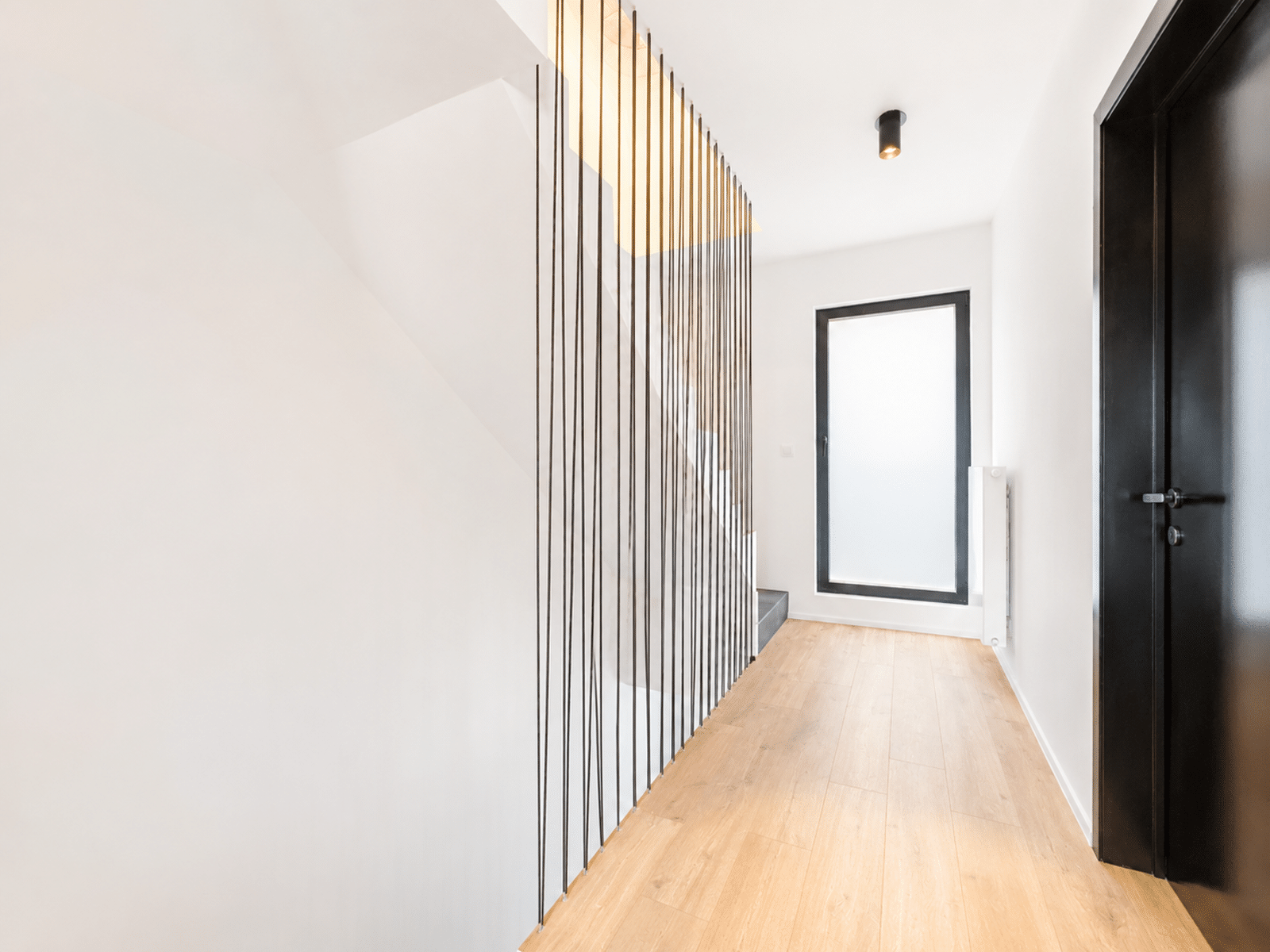 Couloir Moderne avec Escalier – You Real Estate Agency Couloir moderne de maison avec escalier, claustra noir et parquet clair.