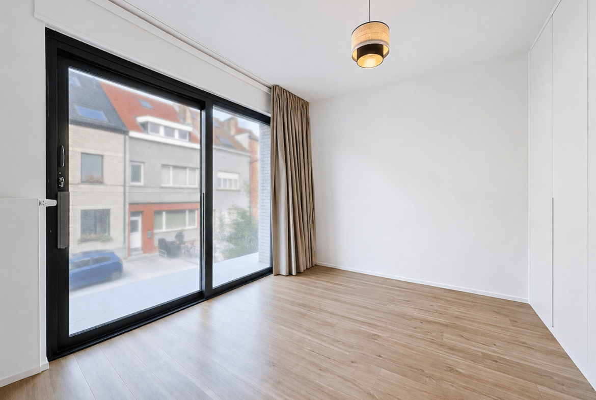 Salon lumineux d’appartement avec baie vitrée, parquet clair et rideaux.