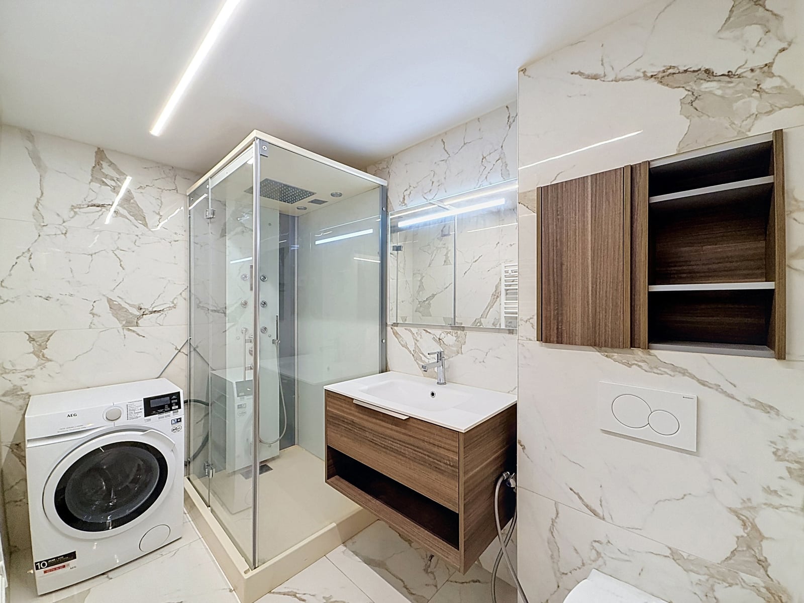 Moderne badkamer met douche - Uw Makelaarskantoor Moderne badkamer met glazen douchewand, wastafelmeubel en wasmachine in een appartement.