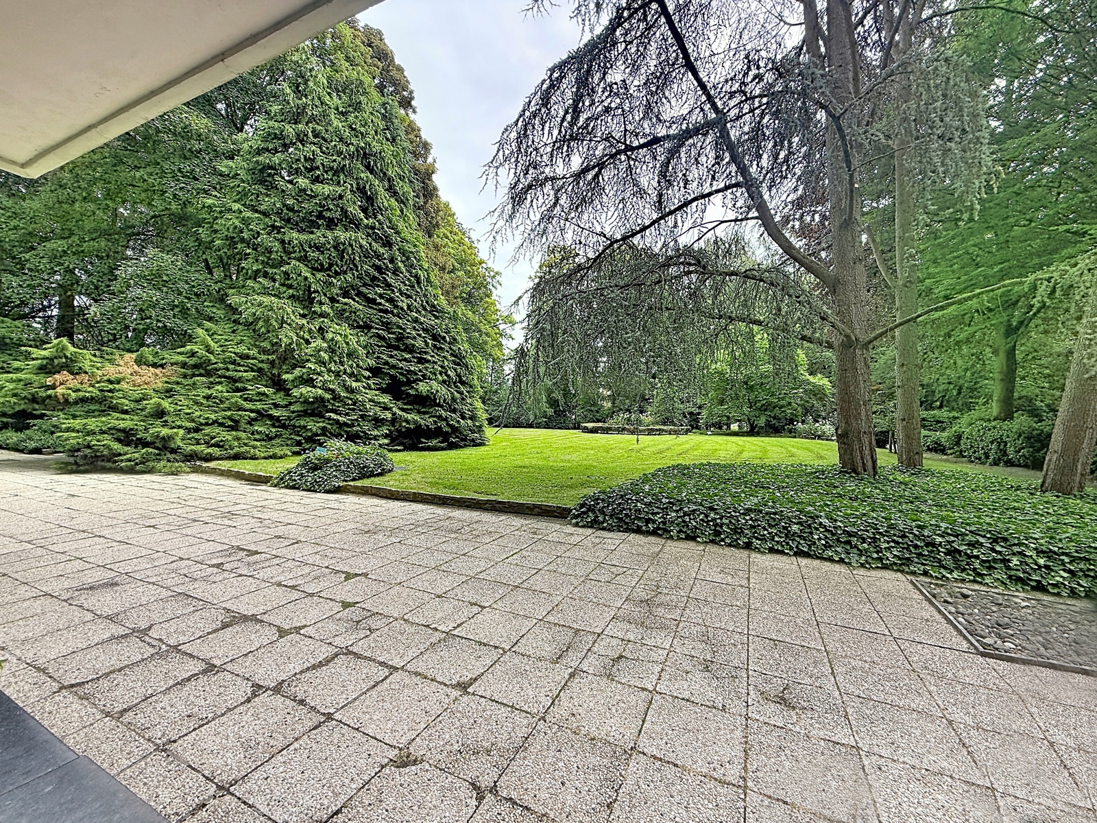 Terras met grote tuin – You Real Estate Agency Ruim terras met een grote, mooi aangelegde tuin bij een luxe woning.