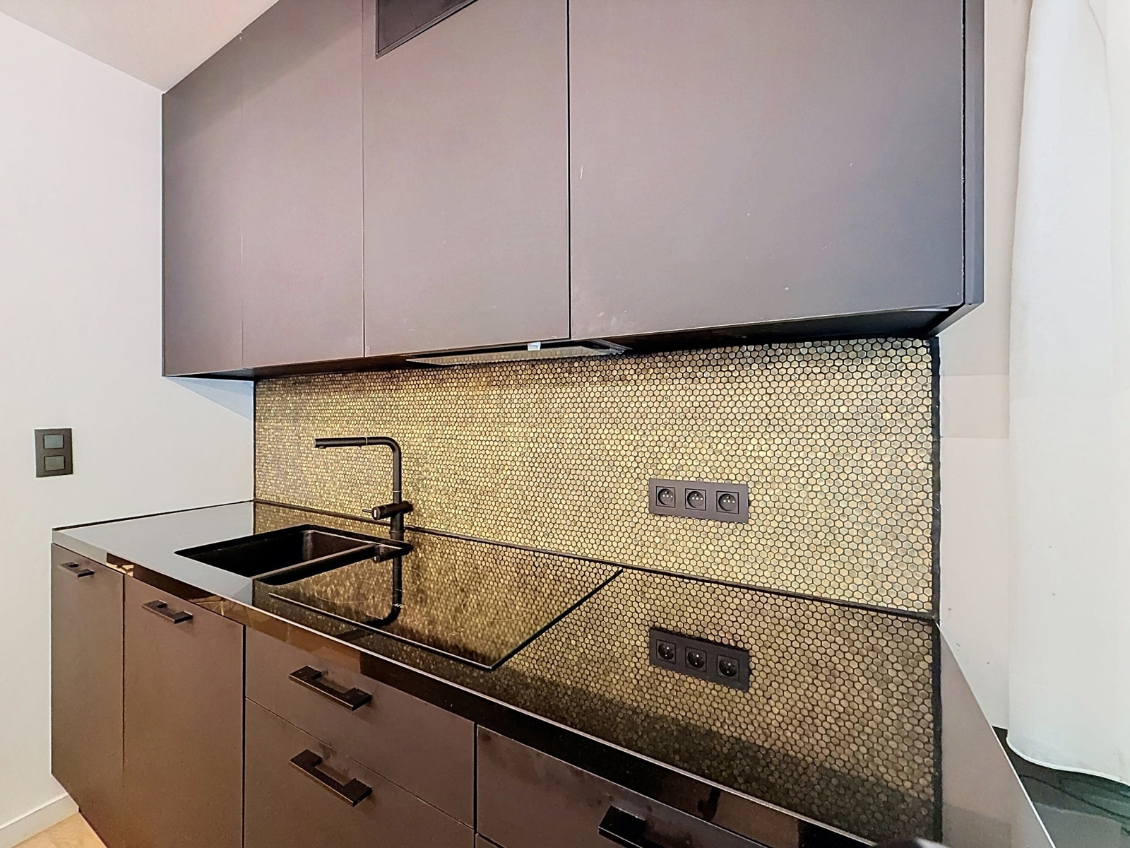 foto 4 Moderne keuken met grijze kasten met vlakke fronten, een zwart werkblad en een achterwand van zeshoekige tegels; een zwarte spoelbak en kraan zijn te zien.