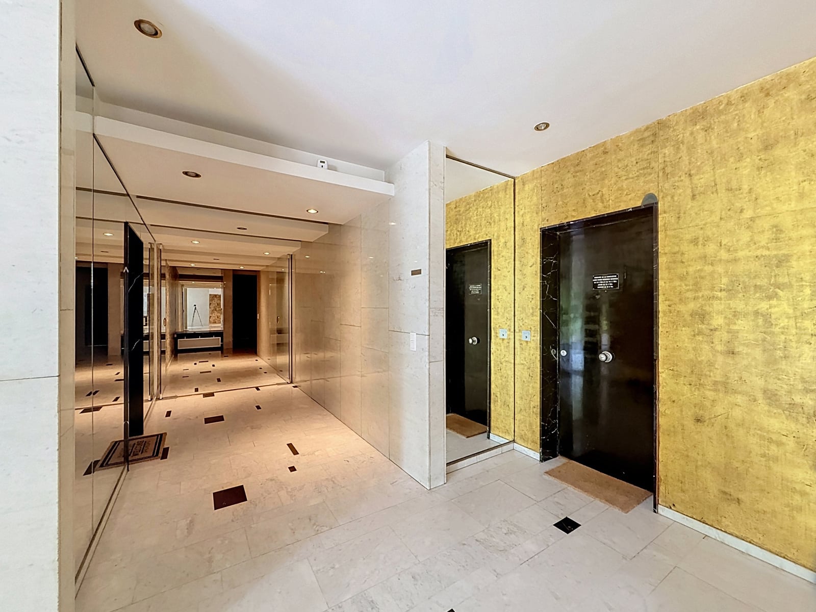 Marmeren entreehal – You Real Estate Agency Elegante entreehal van een flatgebouw met marmer, spiegels en appartementdeuren.