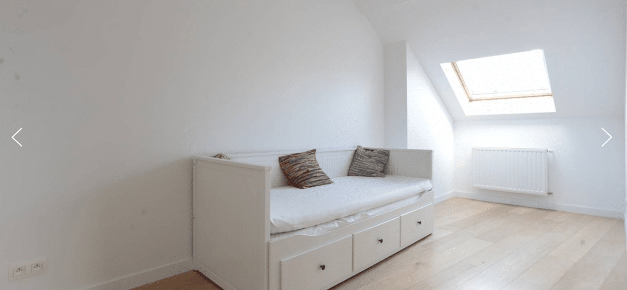 Chambre Mansardée Lumineuse – You Real Estate Agency Chambre mansardée lumineuse d’appartement avec lit banquette, parquet et fenêtre de toit.