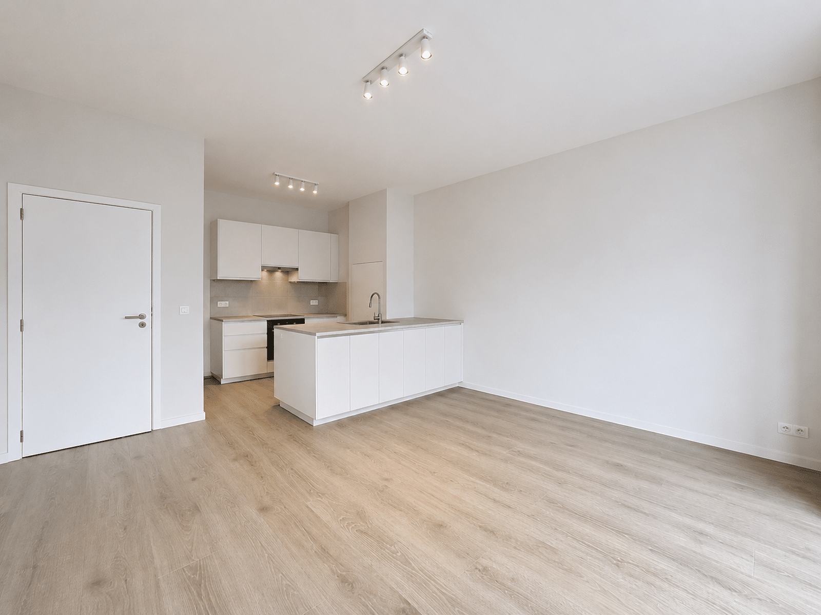 Séjour Lumineux avec Cuisine Ouverte – You Real Estate Agency Appartement moderne avec salon vide, cuisine ouverte blanche et parquet clair.