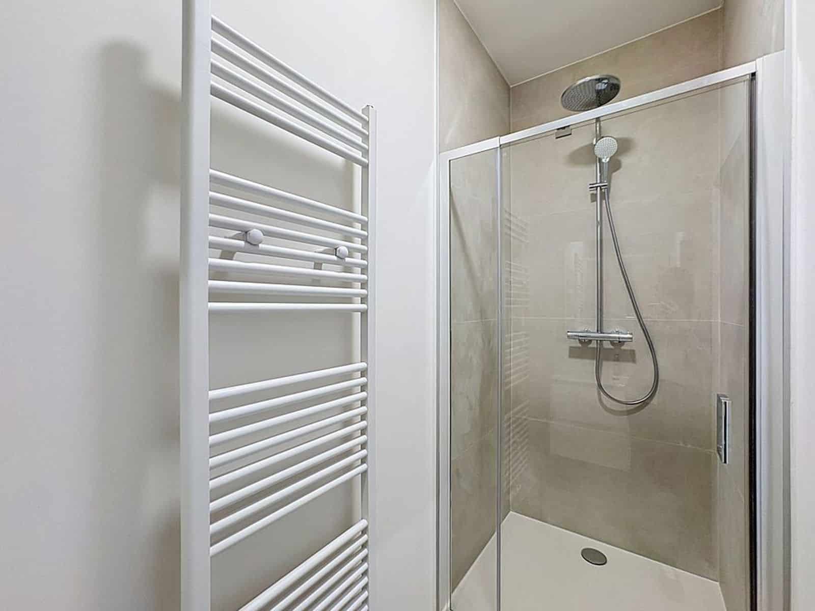 Salle d’Eau avec Douche Vitrée – You Real Estate Agency Salle de bain moderne avec douche vitrée et radiateur sèche-serviettes dans appartement.