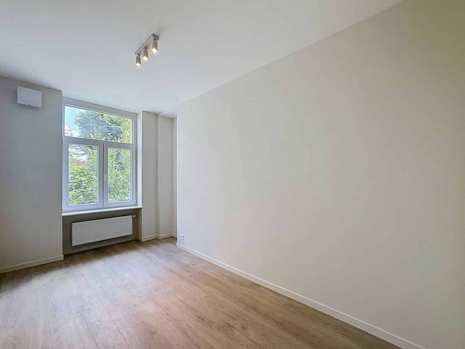 Pièce Lumineuse avec Parquet – You Real Estate Agency Pièce lumineuse d’appartement avec parquet, fenêtre sur verdure et radiateur.
