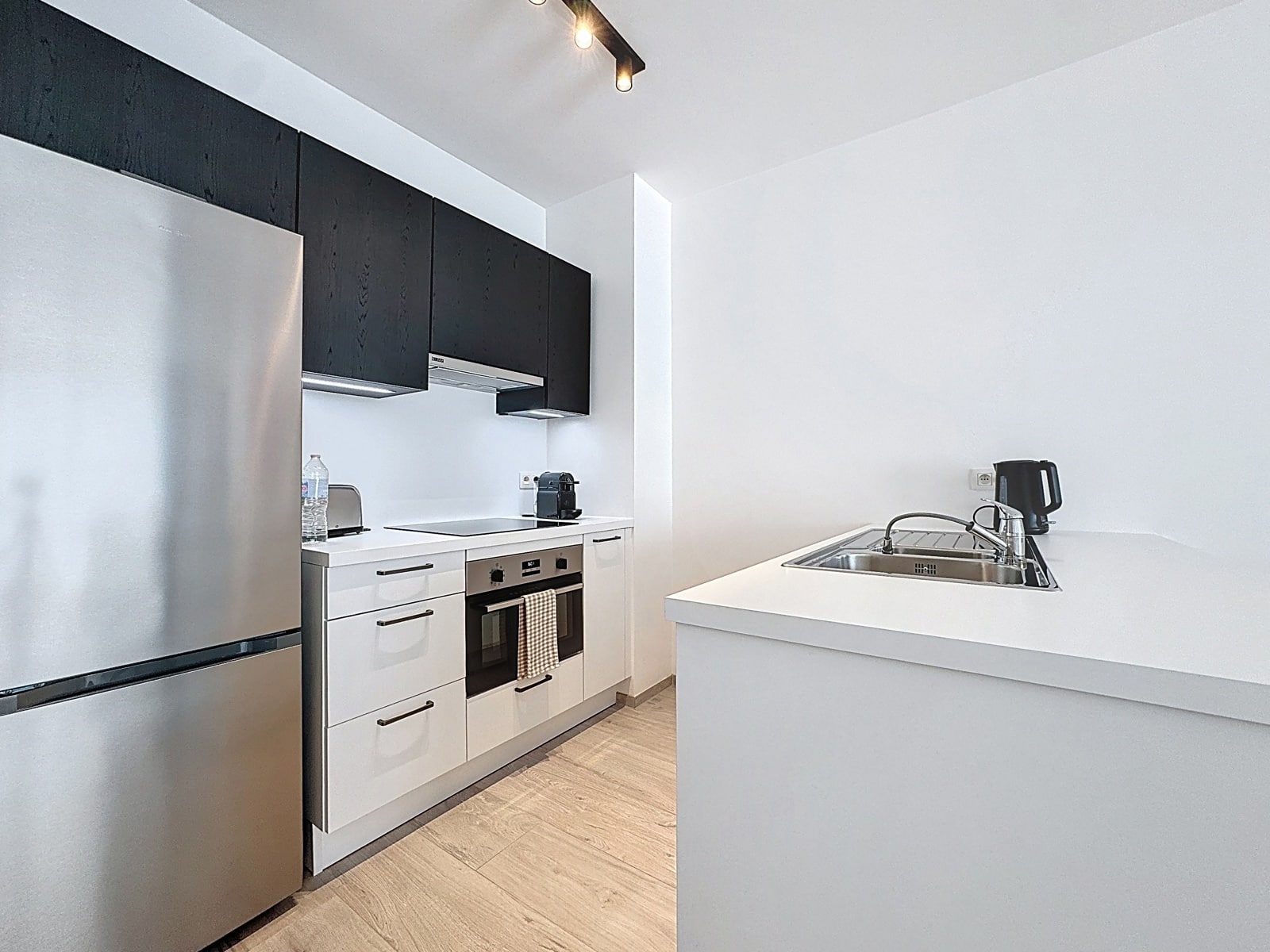 Cuisine Moderne Équipée – You Real Estate Agency Cuisine moderne équipée d’appartement avec électroménagers inox et rangements noirs et blancs.