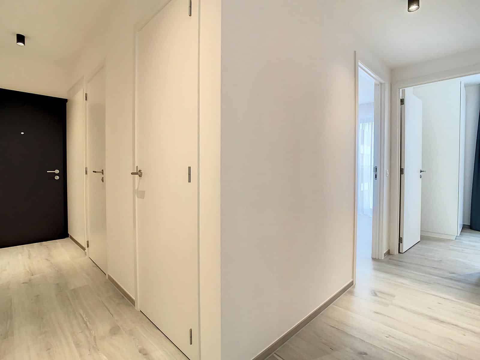 whise photo 11 A white hallway with several closed white doors along one wall and a dark entry door on the far left; light wood floors and minimalist, modern hardware define the space.