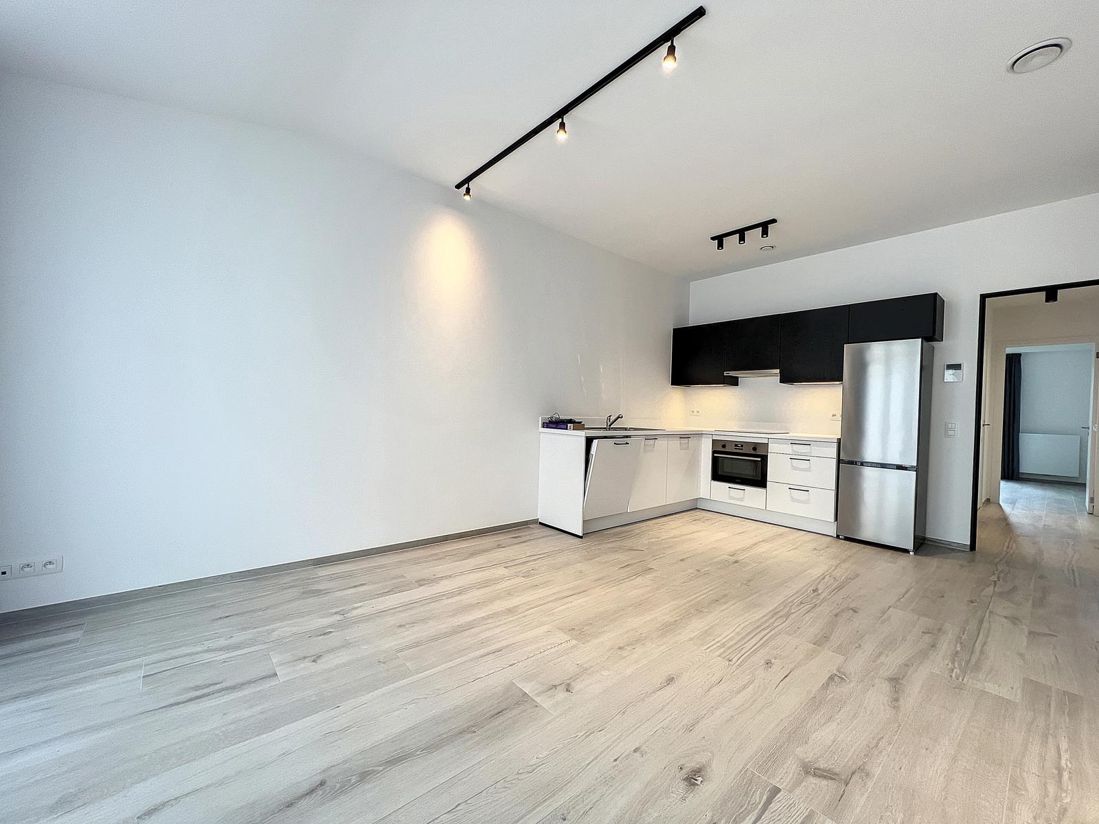 whise photo 2 Open-plan kitchen with white cabinets, black wall cabinets, and stainless fridge along right wall; light wood flooring.
