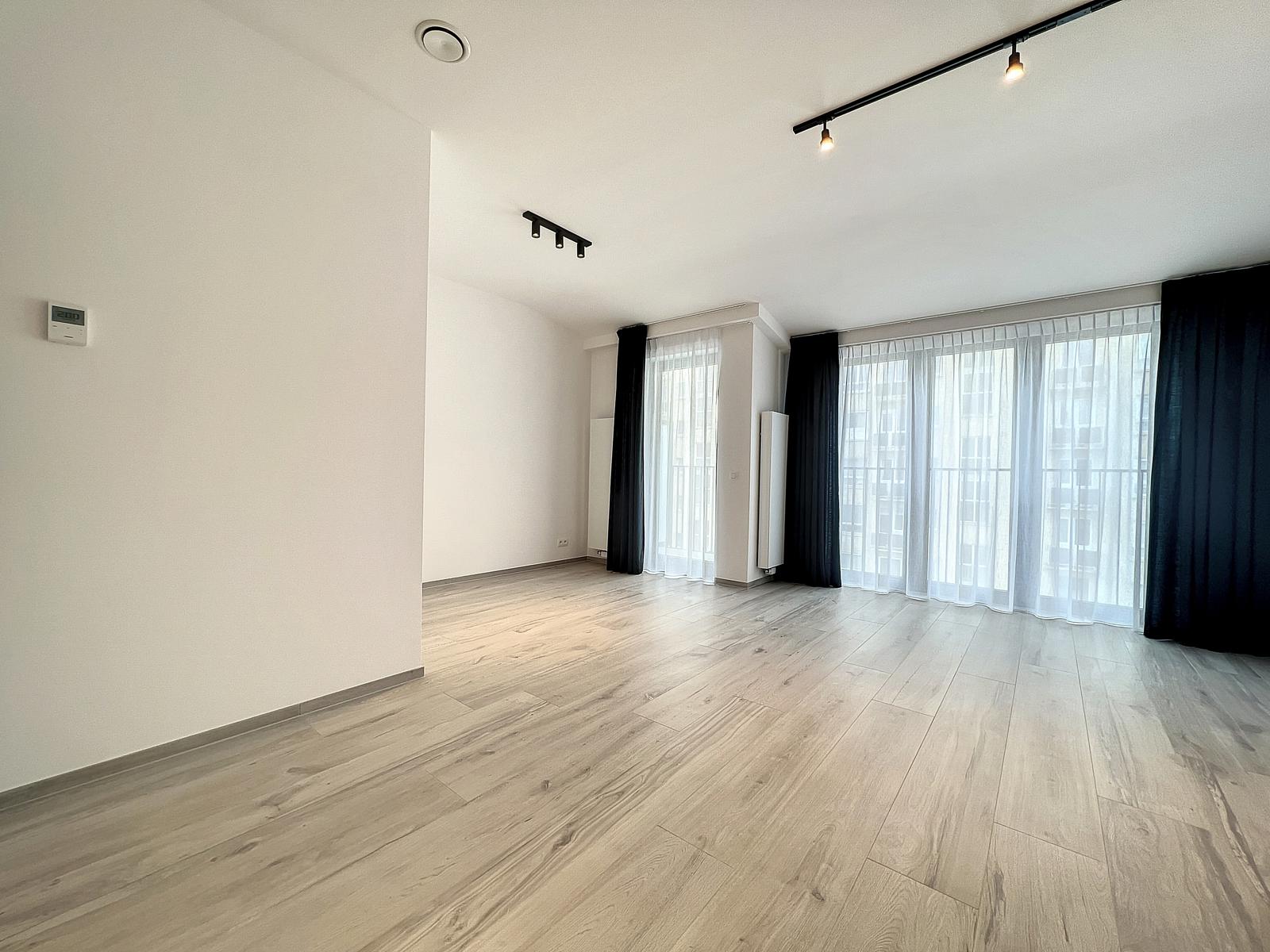 Salon Lumineux d’Appartement Moderne – You Real Estate Agency Salon lumineux d’appartement moderne avec parquet clair, grandes fenêtres et rideaux.