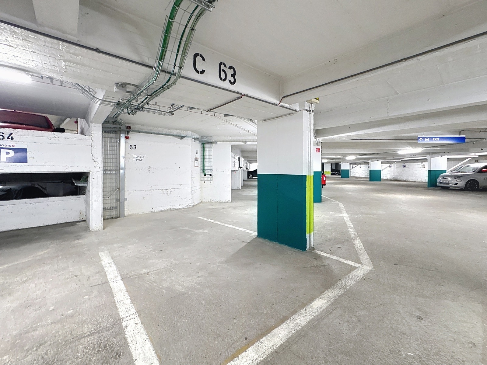 Parking Souterrain Lumineux – You Real Estate Agency Parking souterrain lumineux avec emplacements privatifs et signalisation d’accès.