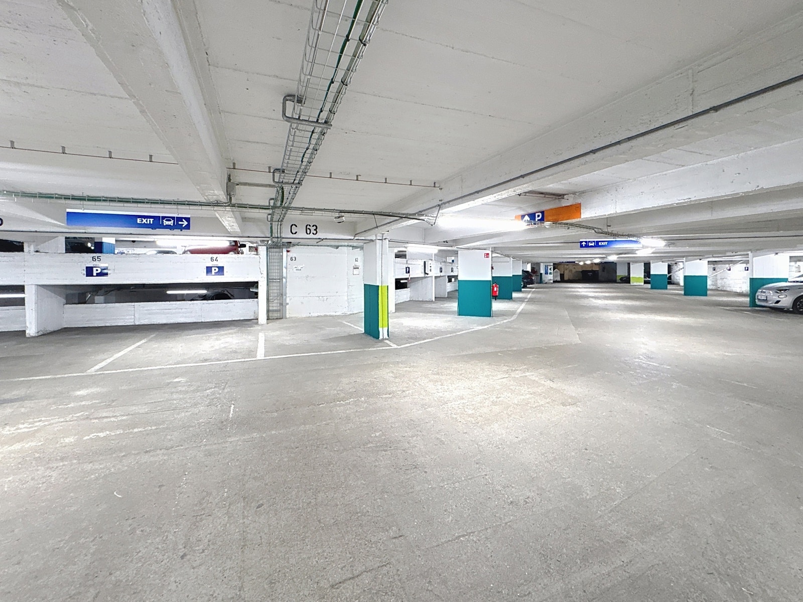 Parking Souterrain Résidentiel – You Real Estate Agency Parking souterrain d’immeuble résidentiel avec places numérotées et signalétique de sortie.