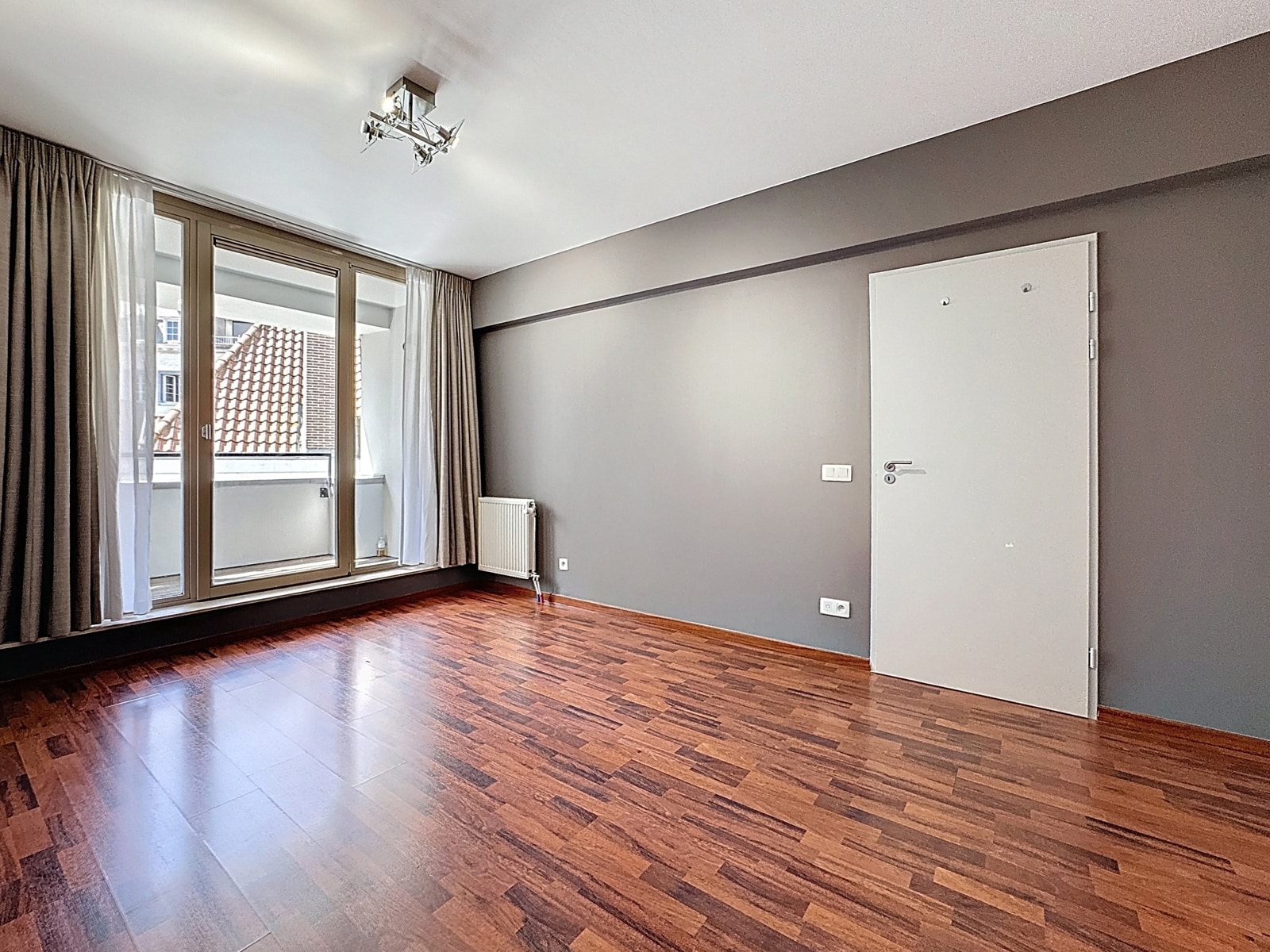 whise photo 6 Empty modern living room with gray walls, dark hardwood floor, and a large balcony door with sheer and heavy curtains.