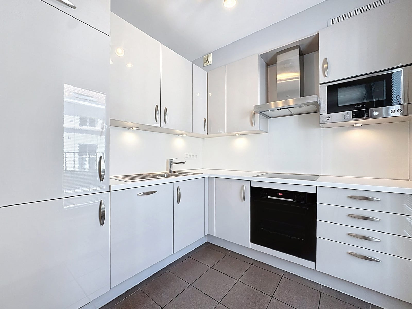 whise photo 4 Modern white L-shaped kitchen with built-in oven, microwave, and glossy cabinets under soft lighting